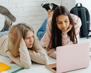 Two teenage girls studying together using a laptop indoors, emphasizing friendship and education.