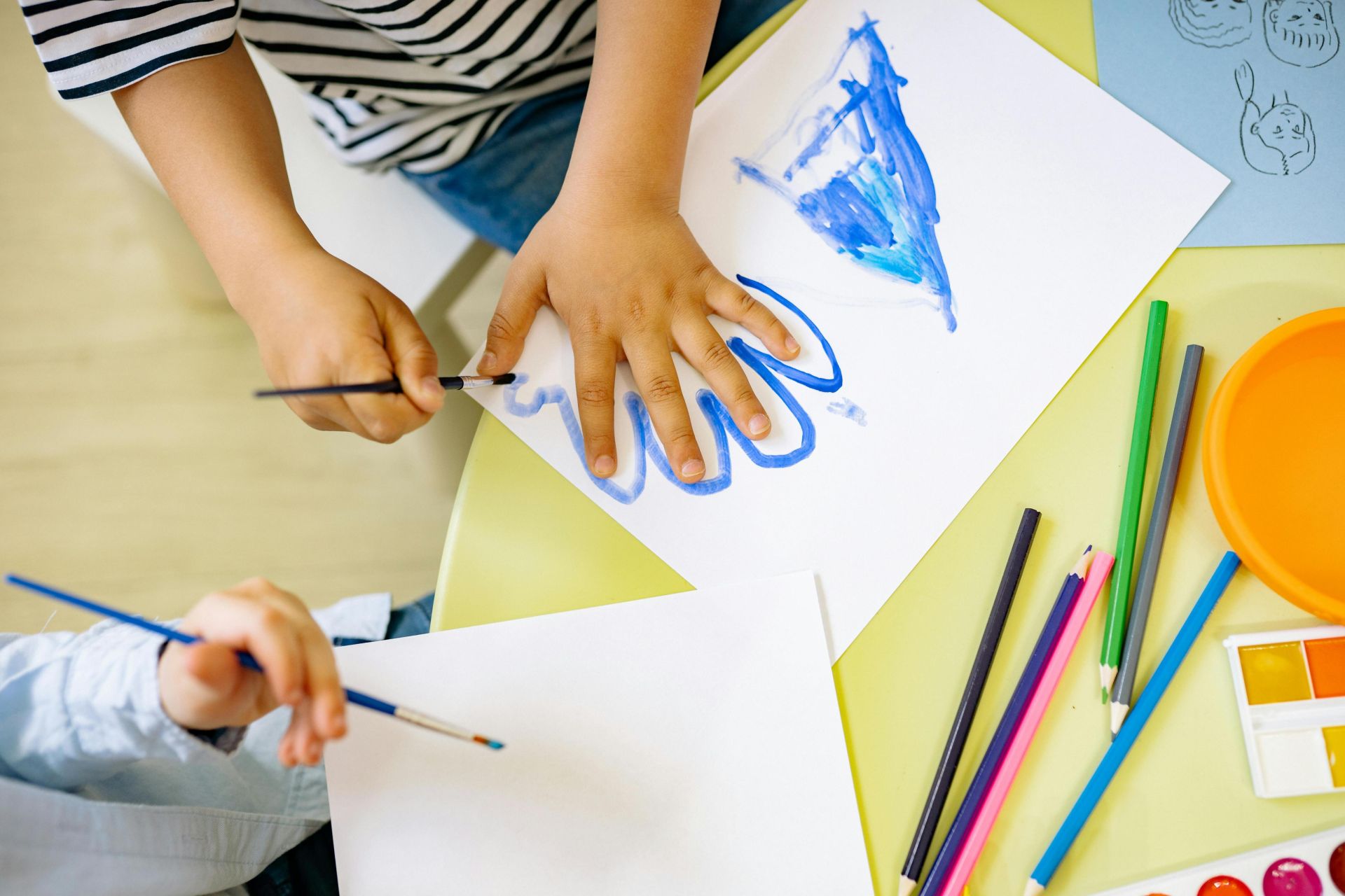 Children painting with watercolors and colored pencils, fostering creativity and learning in a fun environment.